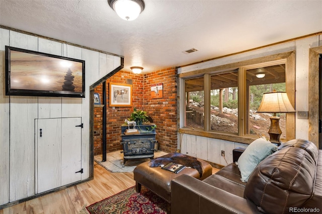 89 Aspen Leaf Ln, Bellvue, CO 80512 - living room featuring a wood stove, light wood-type flooring, brick wall, a textured ceiling, and wooden walls