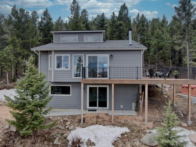 rear view of property featuring a wooded view, a patio area, and a wooden deck