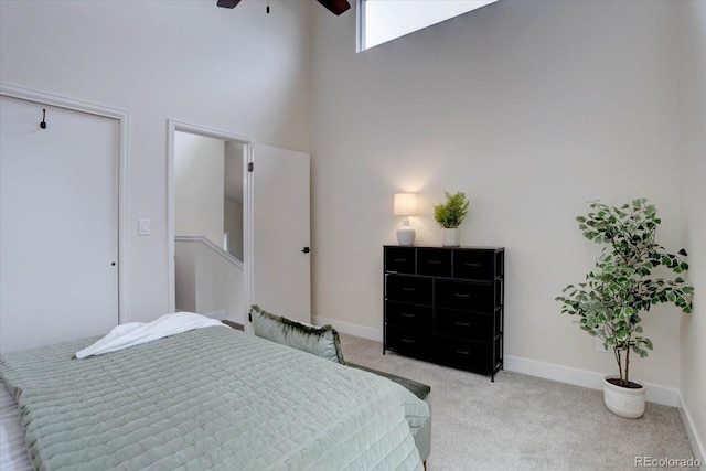bedroom featuring a ceiling fan, a high ceiling, a closet, baseboards, and light carpet