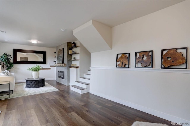 living room featuring stairs, visible vents, dark wood-style flooring, a large fireplace, and baseboards