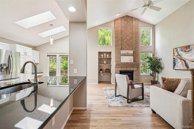 6713 W 98th Cir, Westminster, CO 80021 - living room with a brick fireplace, a skylight, light wood finished floors, high vaulted ceiling, and ceiling fan