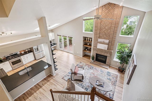 6713 W 98th Cir, Westminster, CO 80021 - living area featuring a ceiling fan, a brick fireplace, high vaulted ceiling, light wood-style flooring, and a skylight