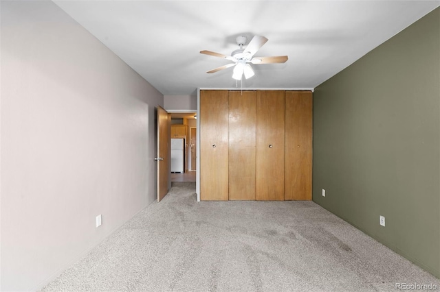 unfurnished bedroom featuring carpet floors, freestanding refrigerator, a closet, and a ceiling fan