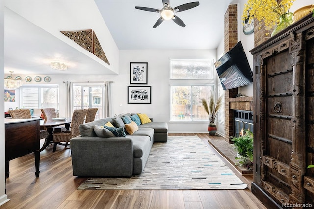 living room with ceiling fan, hardwood / wood-style floors, lofted ceiling, and a brick fireplace