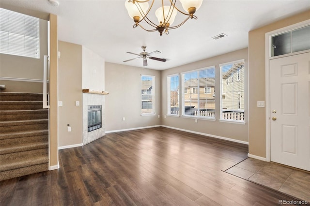 unfurnished living room with visible vents, stairway, ceiling fan with notable chandelier, a fireplace, and wood finished floors