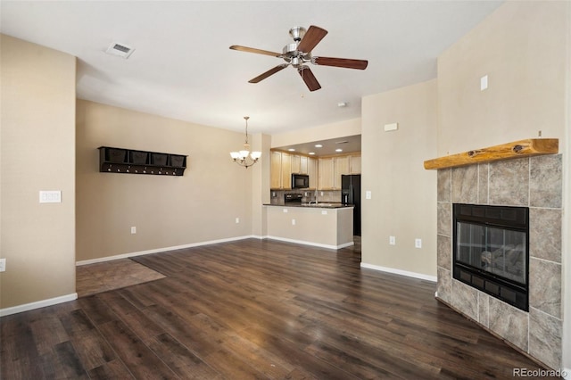 unfurnished living room with baseboards, a tile fireplace, dark wood-style flooring, and ceiling fan with notable chandelier