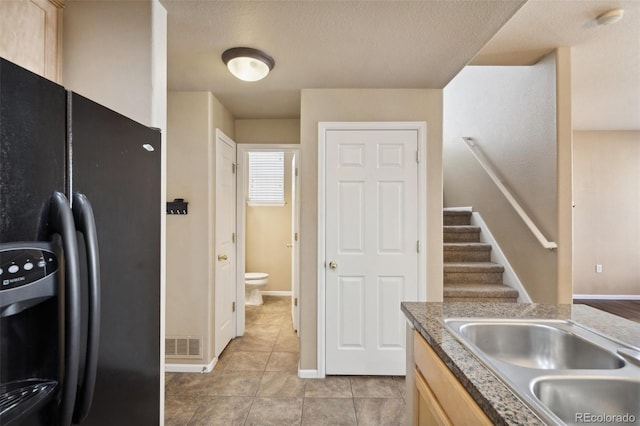 kitchen with light brown cabinets, baseboards, light tile patterned floors, black fridge with ice dispenser, and a sink