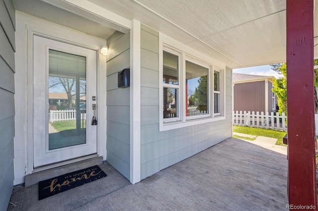 view of exterior entry featuring fence and covered porch