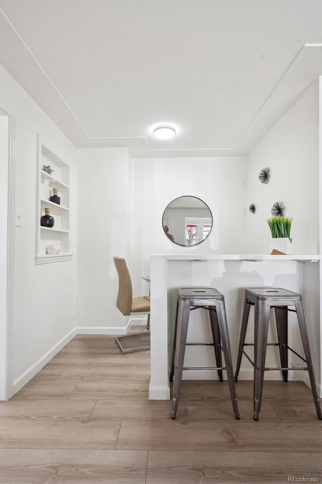 dining space with baseboards, built in shelves, and light wood finished floors