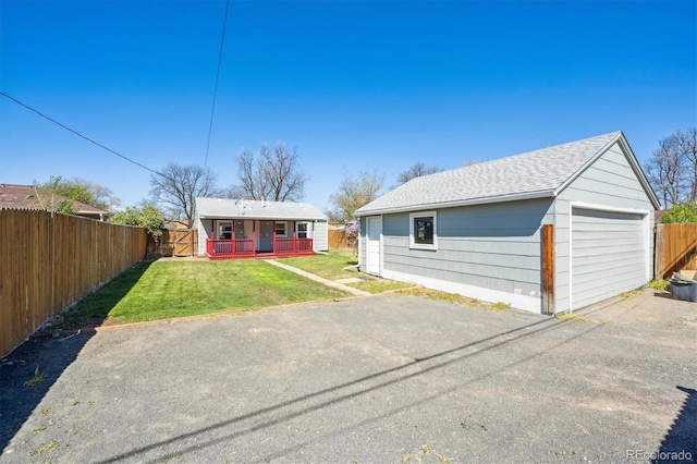 bungalow-style house featuring fence, a front yard, roof with shingles, a porch, and a detached garage