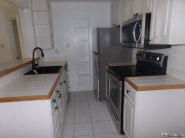 6705 S Field St Unit 802, Littleton, CO 80128 - kitchen with appliances with stainless steel finishes, a sink, white cabinets, light tile patterned flooring, and tile countertops