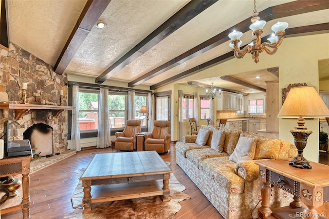 living room with lofted ceiling with beams, a fireplace, a chandelier, and hardwood / wood-style floors