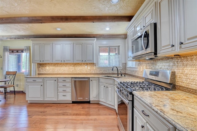 kitchen with sink, white cabinetry, stainless steel appliances, beamed ceiling, and light wood-type flooring