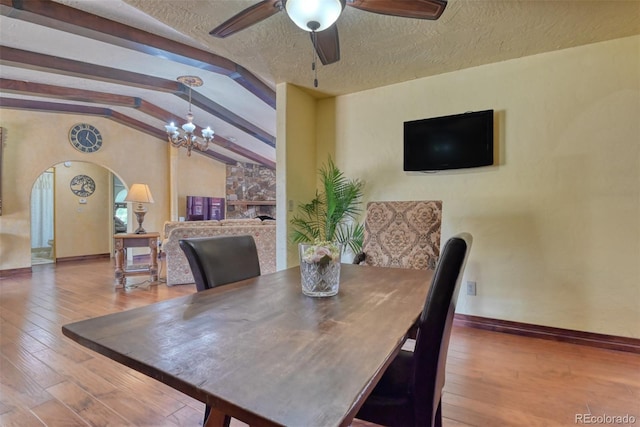 dining space featuring ceiling fan with notable chandelier, a textured ceiling, vaulted ceiling with beams, and hardwood / wood-style flooring