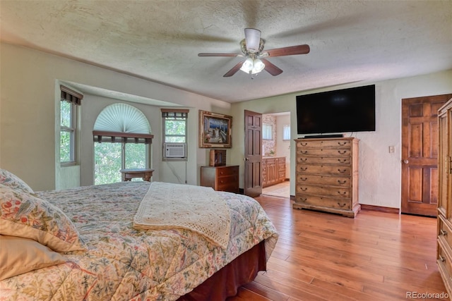 bedroom featuring ensuite bathroom, cooling unit, ceiling fan, light hardwood / wood-style floors, and a textured ceiling