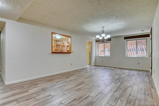 unfurnished room featuring a textured ceiling, an inviting chandelier, and light hardwood / wood-style floors