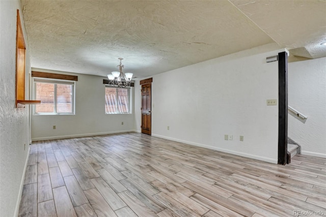 spare room with light hardwood / wood-style floors, a textured ceiling, and a notable chandelier