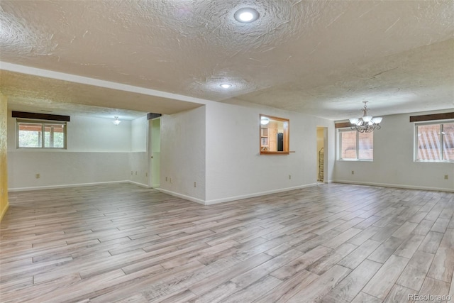 empty room with a notable chandelier, a textured ceiling, and light hardwood / wood-style flooring