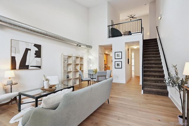 living room with ceiling fan, light hardwood / wood-style floors, and a high ceiling