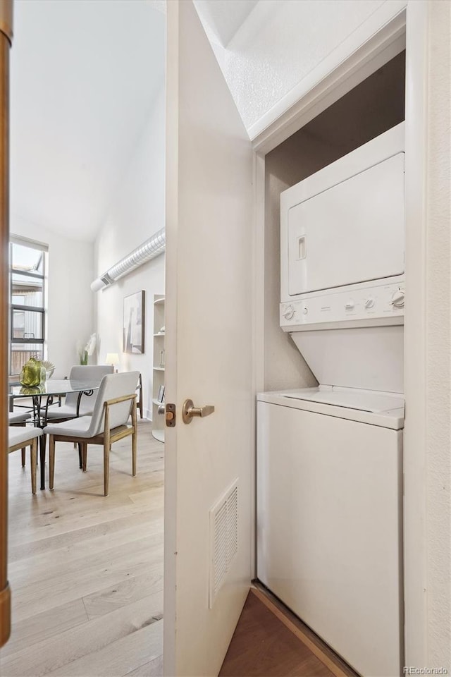 laundry room featuring stacked washer and clothes dryer, a textured ceiling, and light wood-type flooring