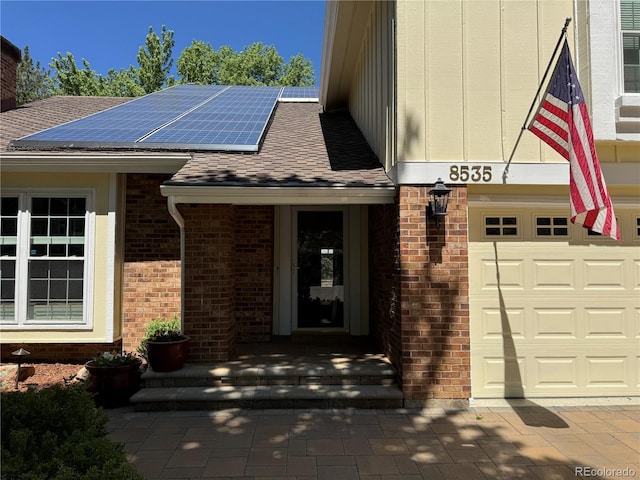 8535 E Otero Cir, Centennial, CO 80112 - doorway to property with roof mounted solar panels, brick siding, roof with shingles, and an attached garage