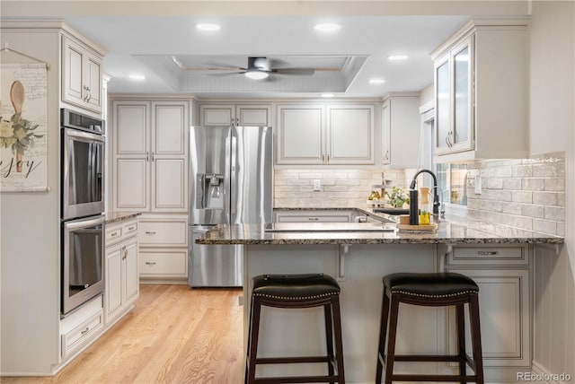 8535 E Otero Cir, Centennial, CO 80112 - kitchen featuring stainless steel appliances, a peninsula, a sink, light wood-style flooring, and decorative backsplash