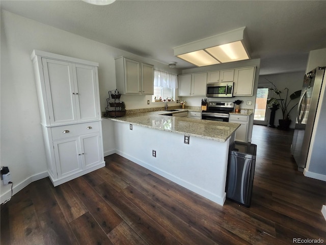 21924 E Lake Ave, Aurora, CO 80015 - kitchen featuring appliances with stainless steel finishes, a peninsula, dark wood-type flooring, light stone countertops, and healthy amount of natural light