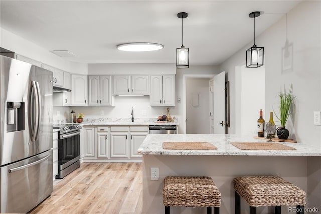 5947 W 65th Ave, Arvada, CO 80003 - kitchen with appliances with stainless steel finishes, a peninsula, a breakfast bar area, light stone countertops, and light wood-type flooring