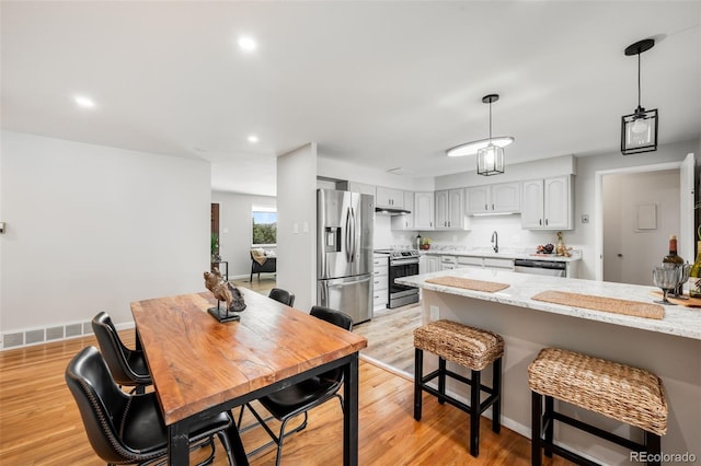 5947 W 65th Ave, Arvada, CO 80003 - kitchen featuring appliances with stainless steel finishes, a breakfast bar area, hanging light fixtures, light wood finished floors, and white cabinetry