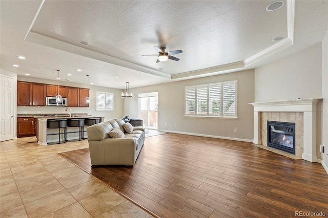 4545 Oxbow Dr, Brighton, CO 80601 - living area featuring a raised ceiling, ceiling fan, a fireplace, wood finished floors, and baseboards