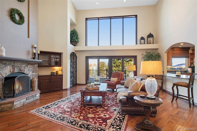 living room with a stone fireplace, wood-type flooring, and a high ceiling