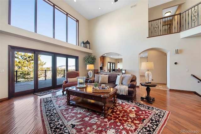 living room with wood-type flooring, a towering ceiling, and french doors