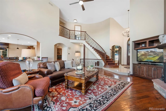 living room featuring dark hardwood / wood-style flooring, ceiling fan with notable chandelier, and a high ceiling