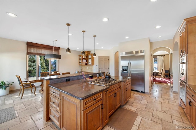 kitchen featuring appliances with stainless steel finishes, a kitchen island with sink, pendant lighting, and dark stone counters