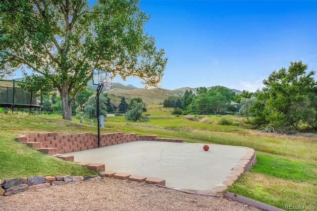 exterior space with basketball hoop, a mountain view, a trampoline, and a lawn