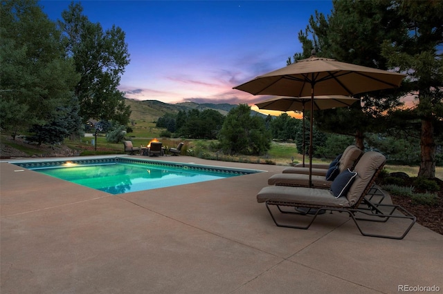 pool at dusk featuring a mountain view and a patio area