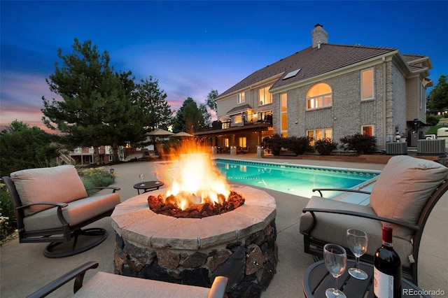 pool at dusk with central AC, a patio area, and a fire pit