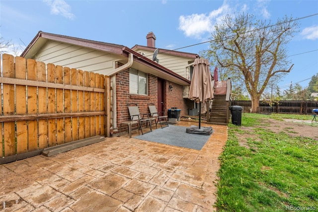 rear view of property featuring a patio area, a fenced backyard, brick siding, a chimney, and stairway
