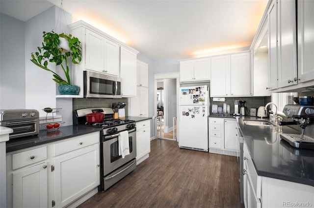 kitchen featuring appliances with stainless steel finishes, sink, white cabinets, dark hardwood / wood-style flooring, and decorative backsplash