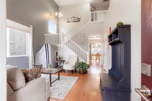 living area with stairs, light wood-type flooring, a towering ceiling, and a notable chandelier