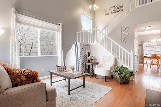 living area featuring a towering ceiling, baseboards, stairs, hardwood / wood-style floors, and an inviting chandelier