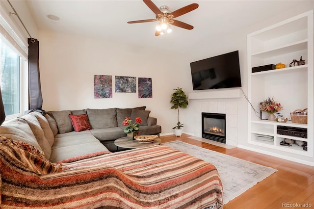 living room featuring ceiling fan, built in shelves, wood finished floors, and a tile fireplace