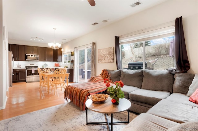 living room with light wood-type flooring, visible vents, and ceiling fan with notable chandelier