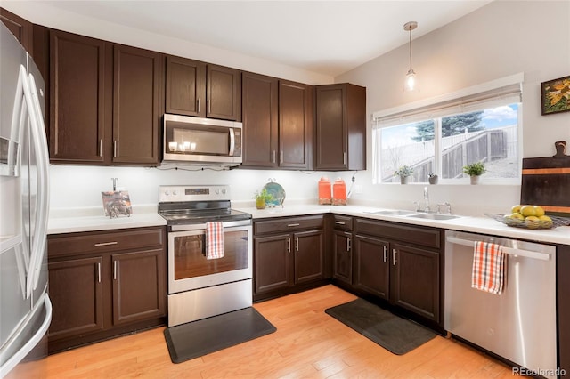 kitchen featuring stainless steel appliances, light wood finished floors, a sink, and light countertops