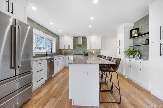 kitchen with appliances with stainless steel finishes, wall chimney exhaust hood, a kitchen bar, decorative backsplash, and open shelves