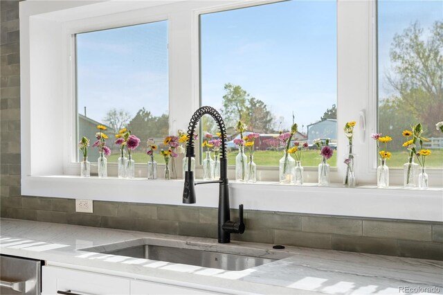 kitchen view of a sink, white cabinets, and light stone counters