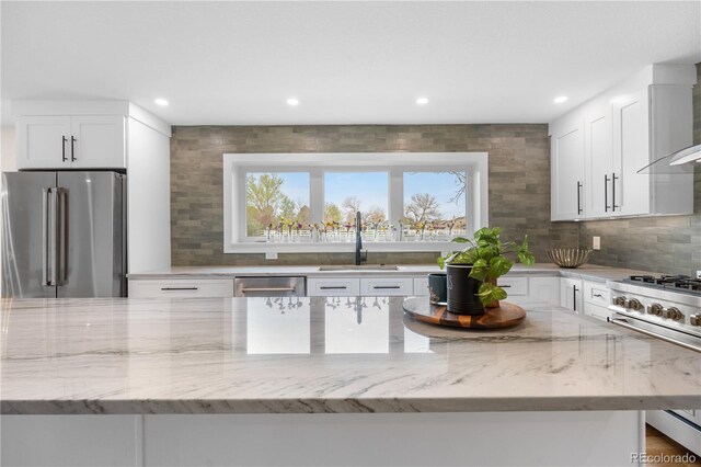 kitchen with high end appliances, a sink, light stone counters, backsplash, and white cabinets