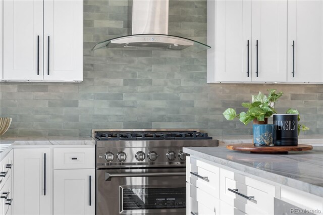 kitchen featuring wall chimney range hood, high end stainless steel range oven, decorative backsplash, and light stone counters