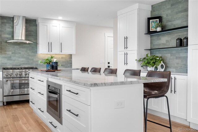 kitchen with wall chimney exhaust hood, stainless steel appliances, a breakfast bar area, light stone countertops, and recessed lighting