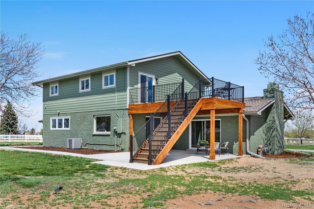 back of property featuring stairway, brick siding, a wooden deck, a patio, and a chimney